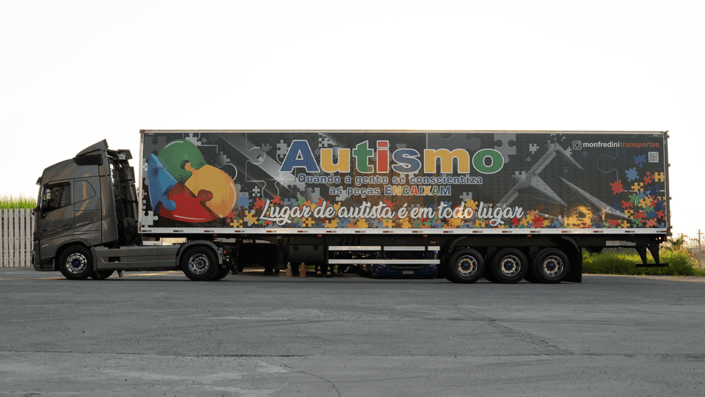 Caminhão da Monfredini Transportes com trailer decorado com peças de quebra-cabeça coloridas promovendo inclusão de pessoas com autismo