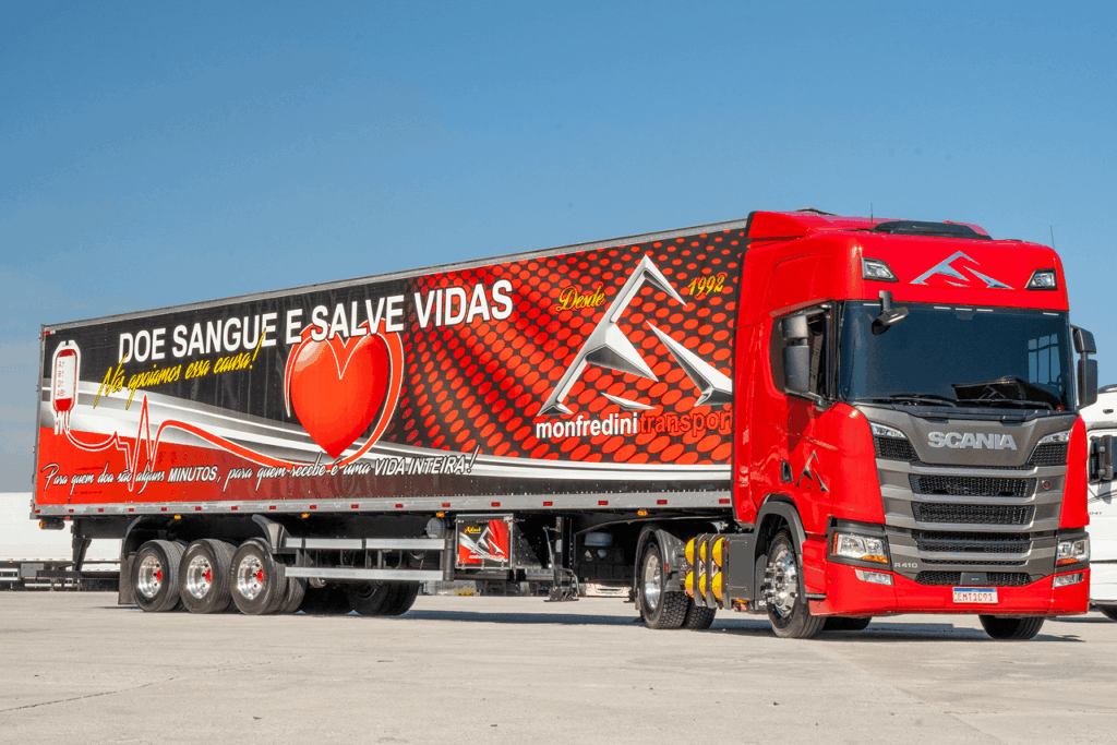 Caminhão Scania vermelho da Monfredini Transportes com trailer preto e vermelho incentivando a doação de sangue